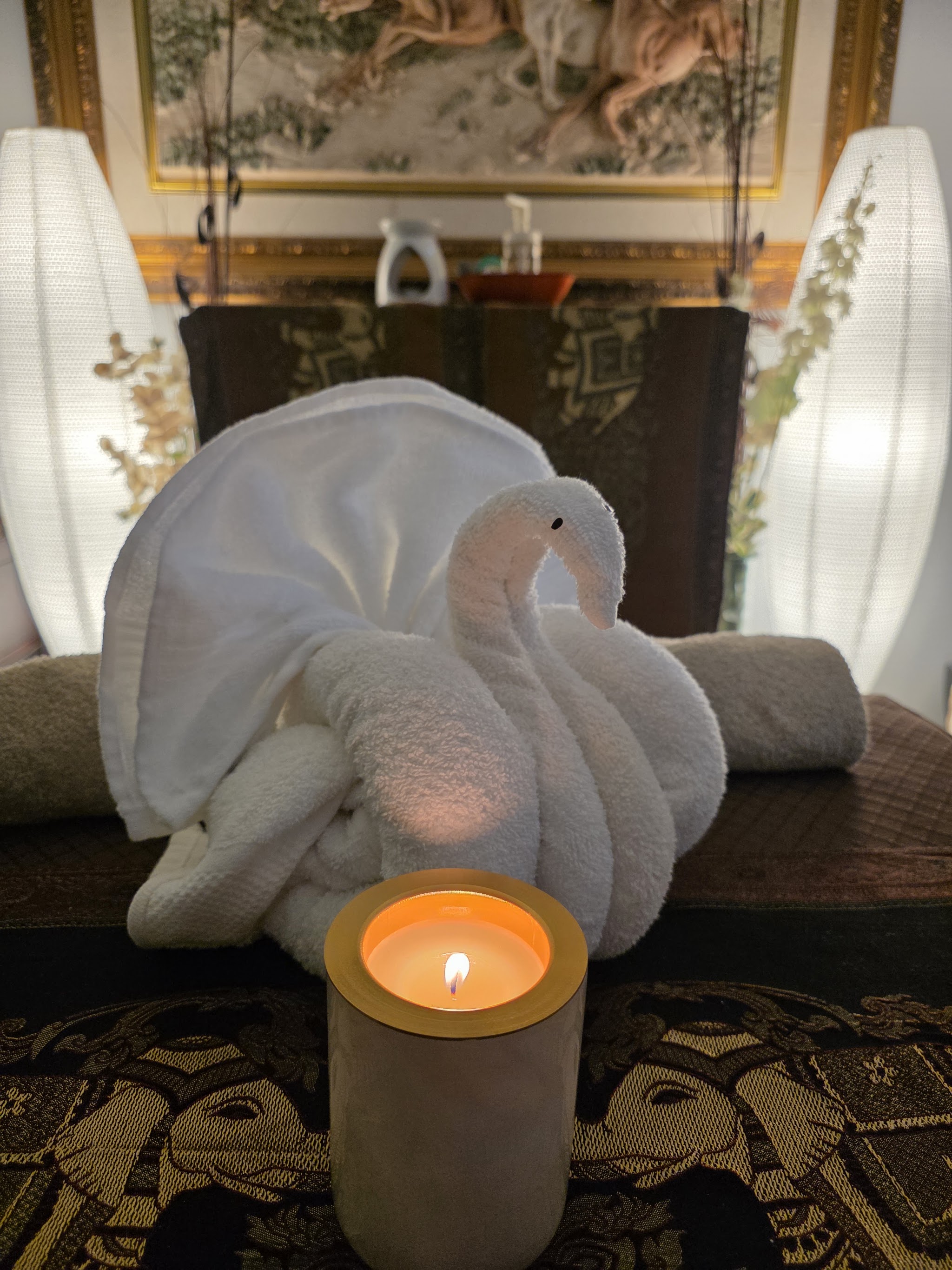 Close up of a towel swan and a glowing candle on the treatment table