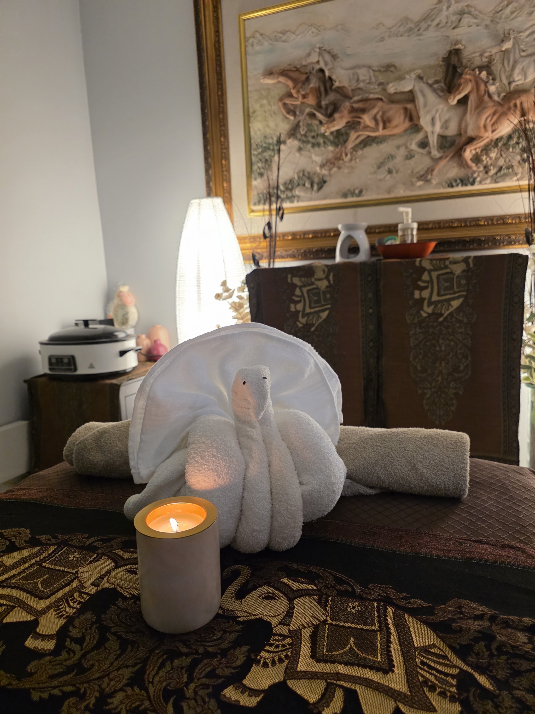 A white towel folded into a swan beside a lit candle on the massage table