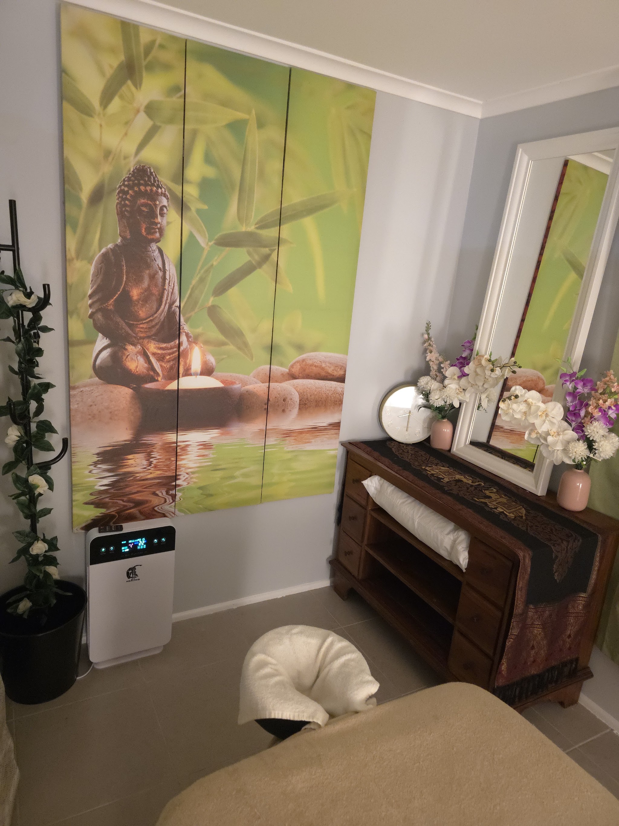 Buddha and bamboo wall mural beside a wooden dresser with orchids and a white mirror