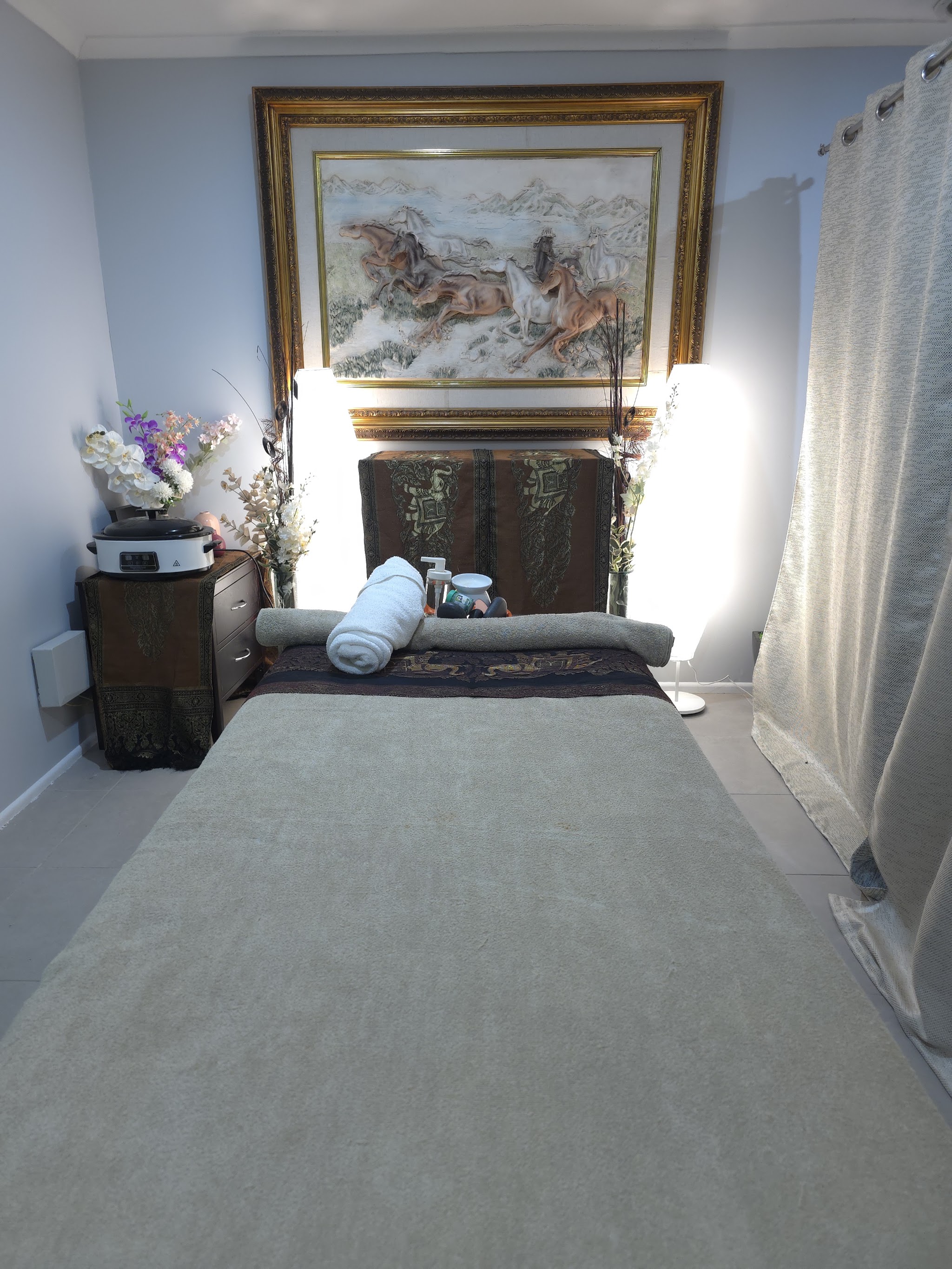 Massage table dressed with rolled towels beneath a gold-framed horse relief artwork