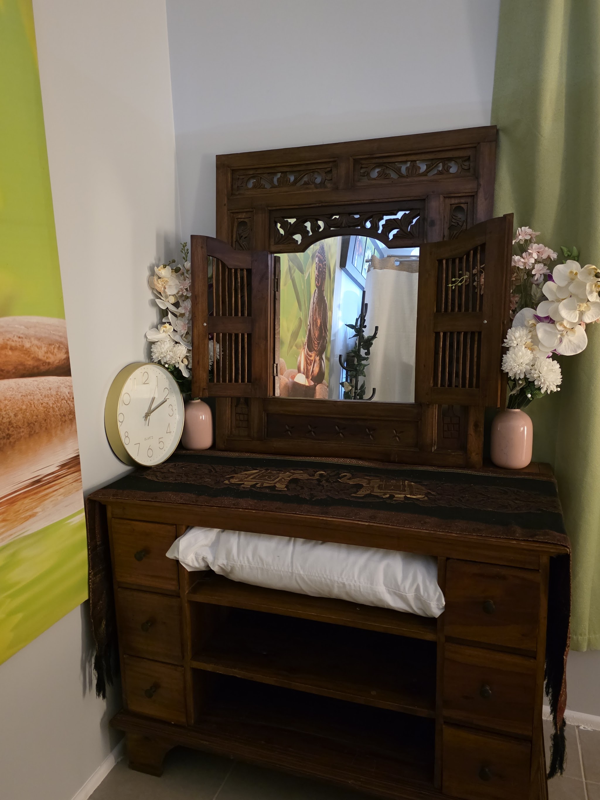 Carved timber mirror with shutters on a wooden chest, with orchids and a gold clock