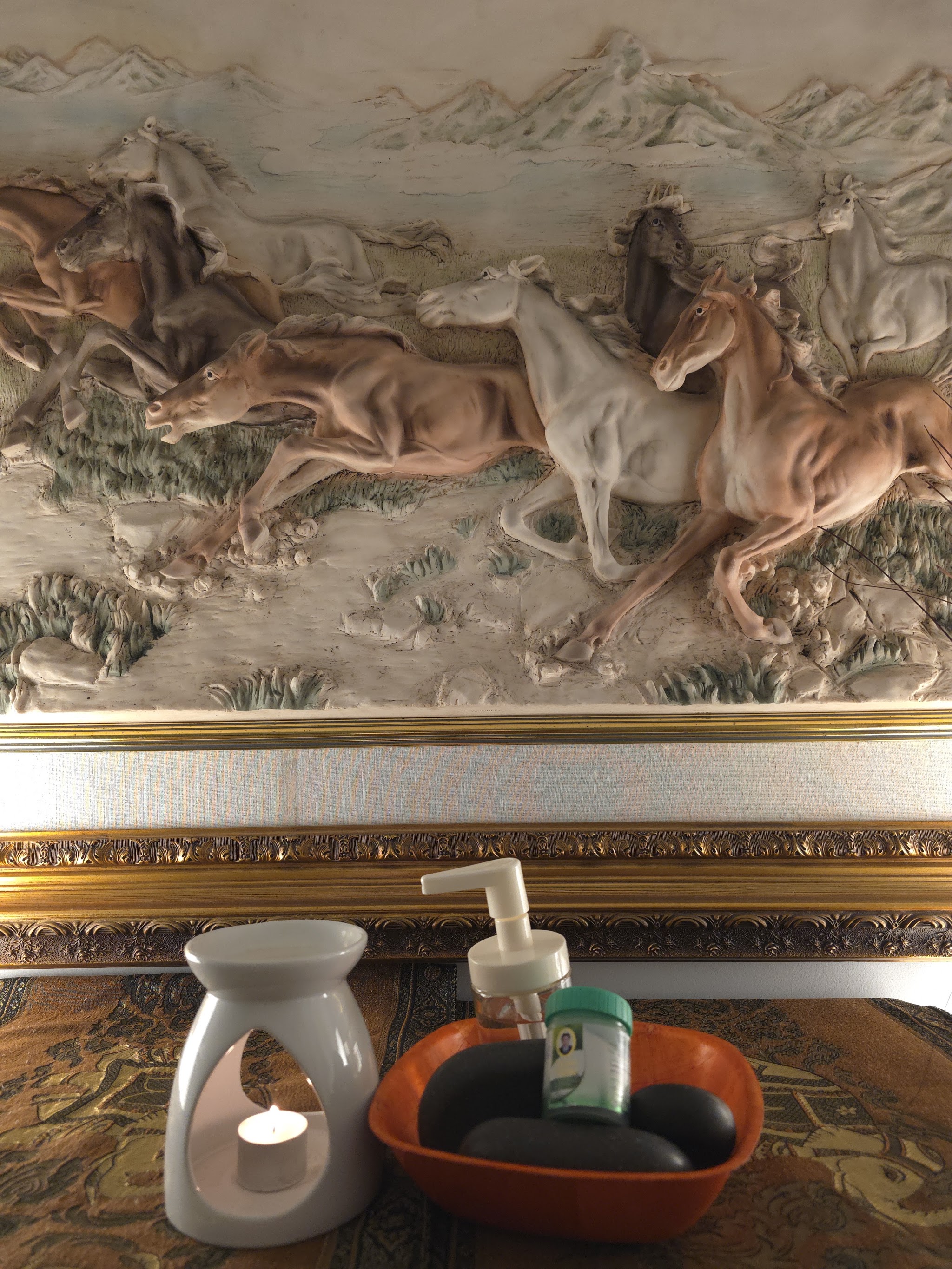 Oil burner with a lit tealight and a bowl of smooth dark stones below a carved horse artwork